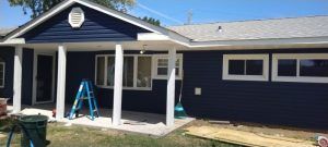 A blue house with white trim and a porch is being painted.