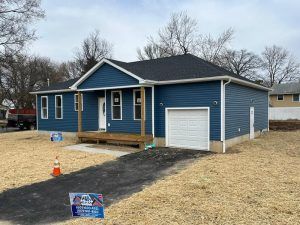 A blue house with a garage and a sign in front of it.
