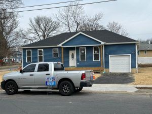 A silver truck is parked in front of a blue house.