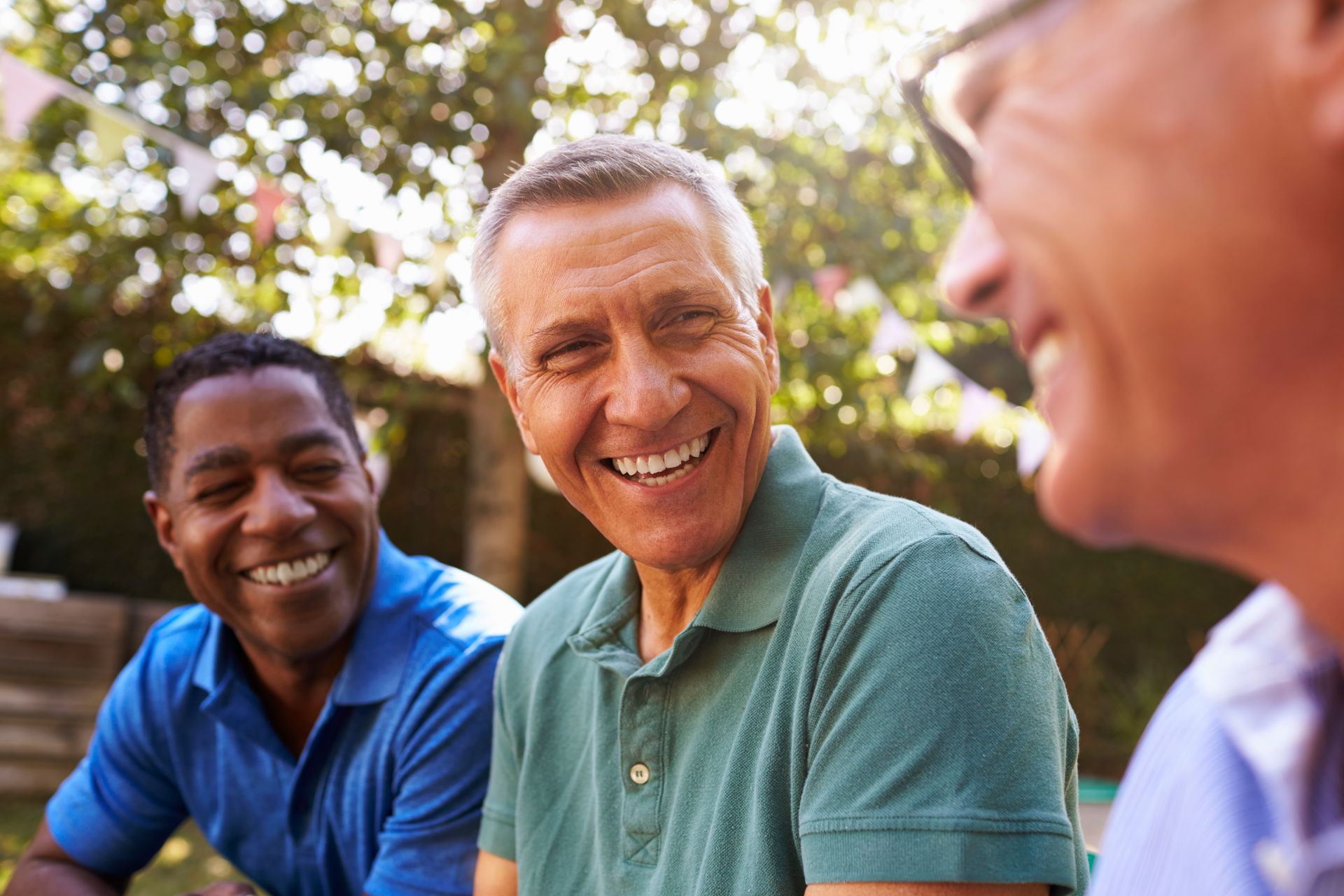 Three smiling men in a sunny outdoor setting; two are African-American, one is Caucasian.