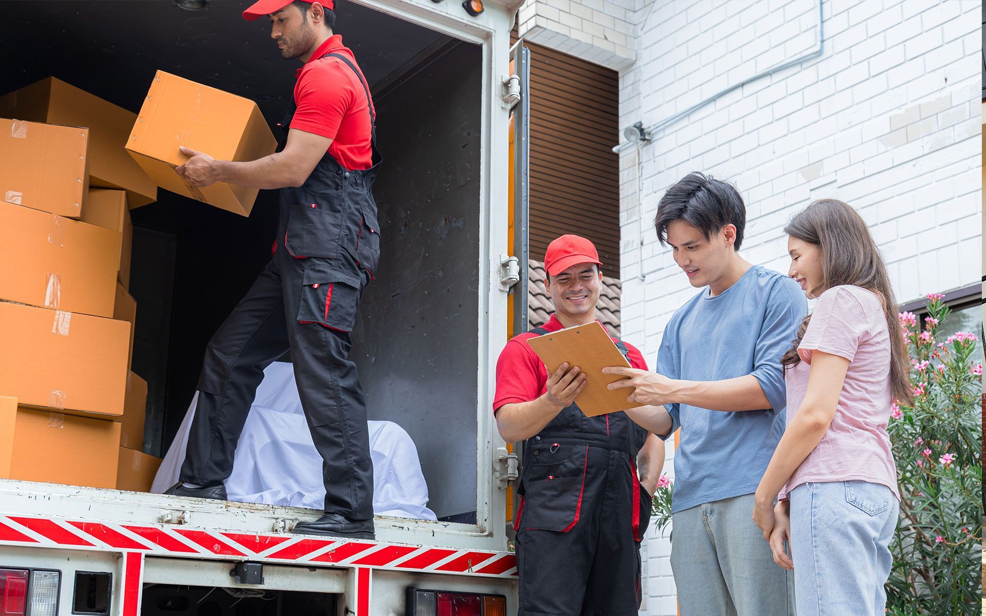 Movers unloading boxes from a truck as a couple reviews paperwork.
