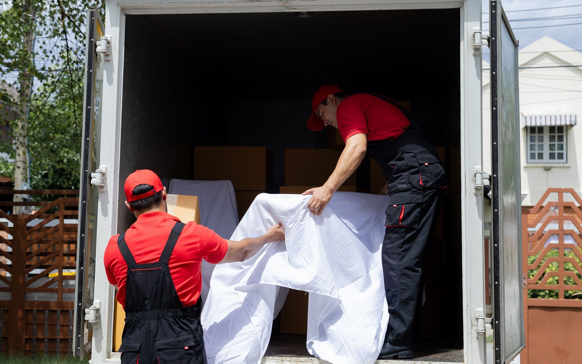 Two movers in red shirts and black overalls loading furniture into a moving truck.