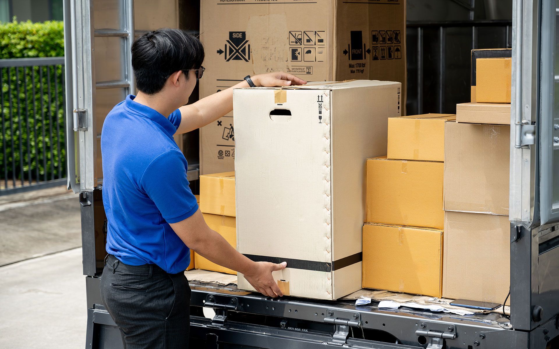 A person in blue shirt loading a large cardboard box into a truck filled with other boxes.