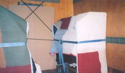 Boxes covered in fabric and cardboard, secured with blue straps and black bungee cords, inside a vehicle.