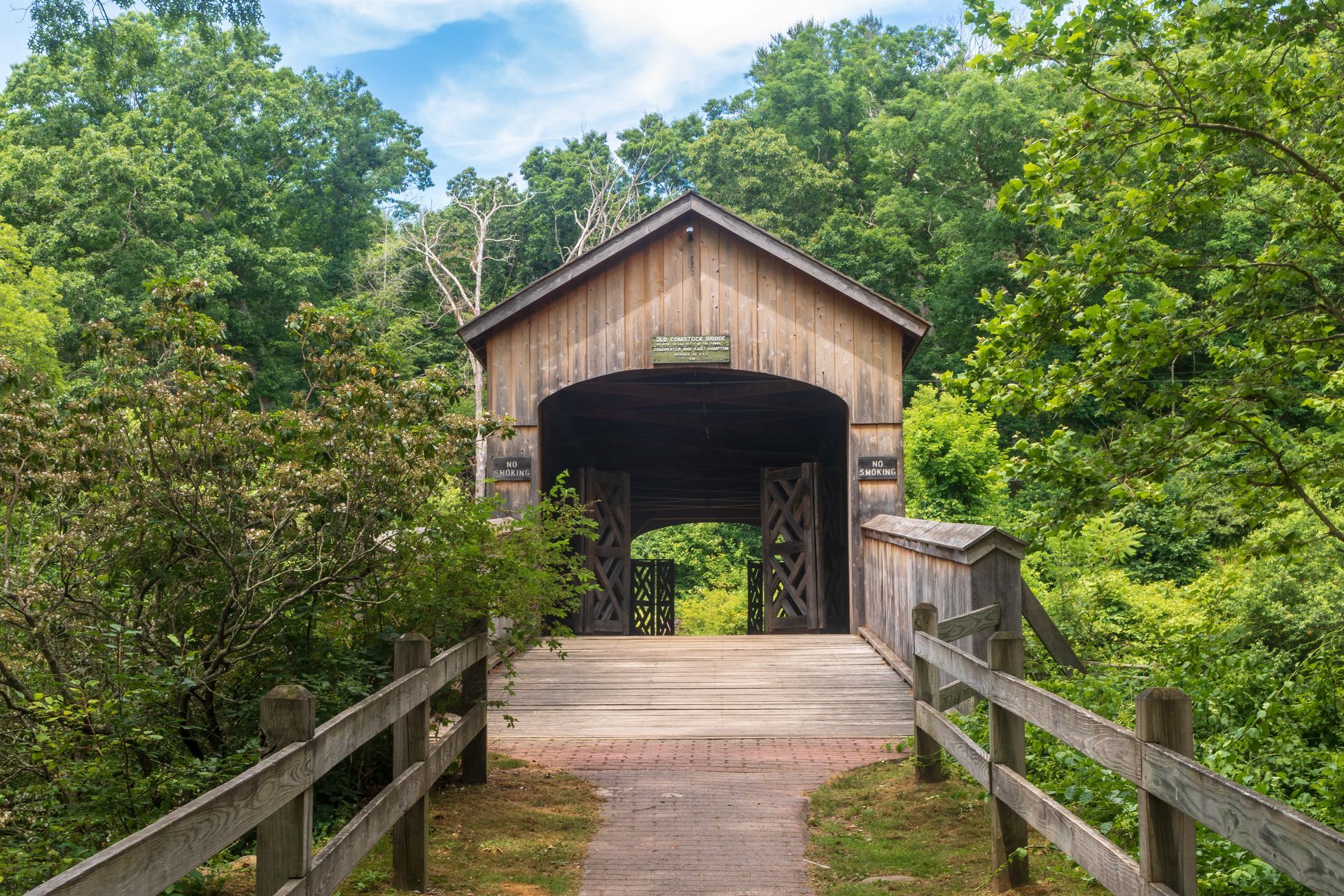 A wooden covered bridge is surrounded by trees and a wooden fence.