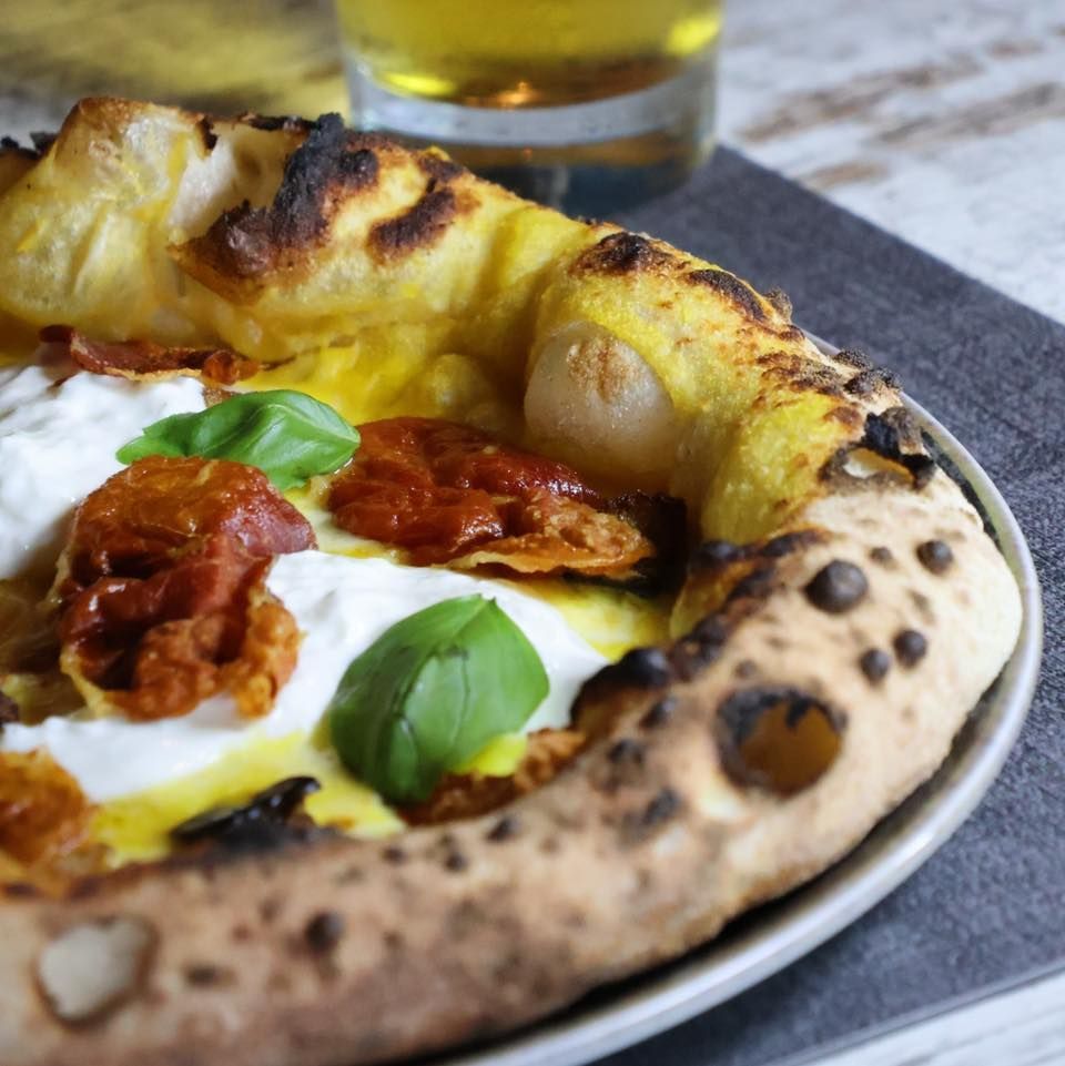 Una pizza su un piatto con un bicchiere di birra sullo sfondo