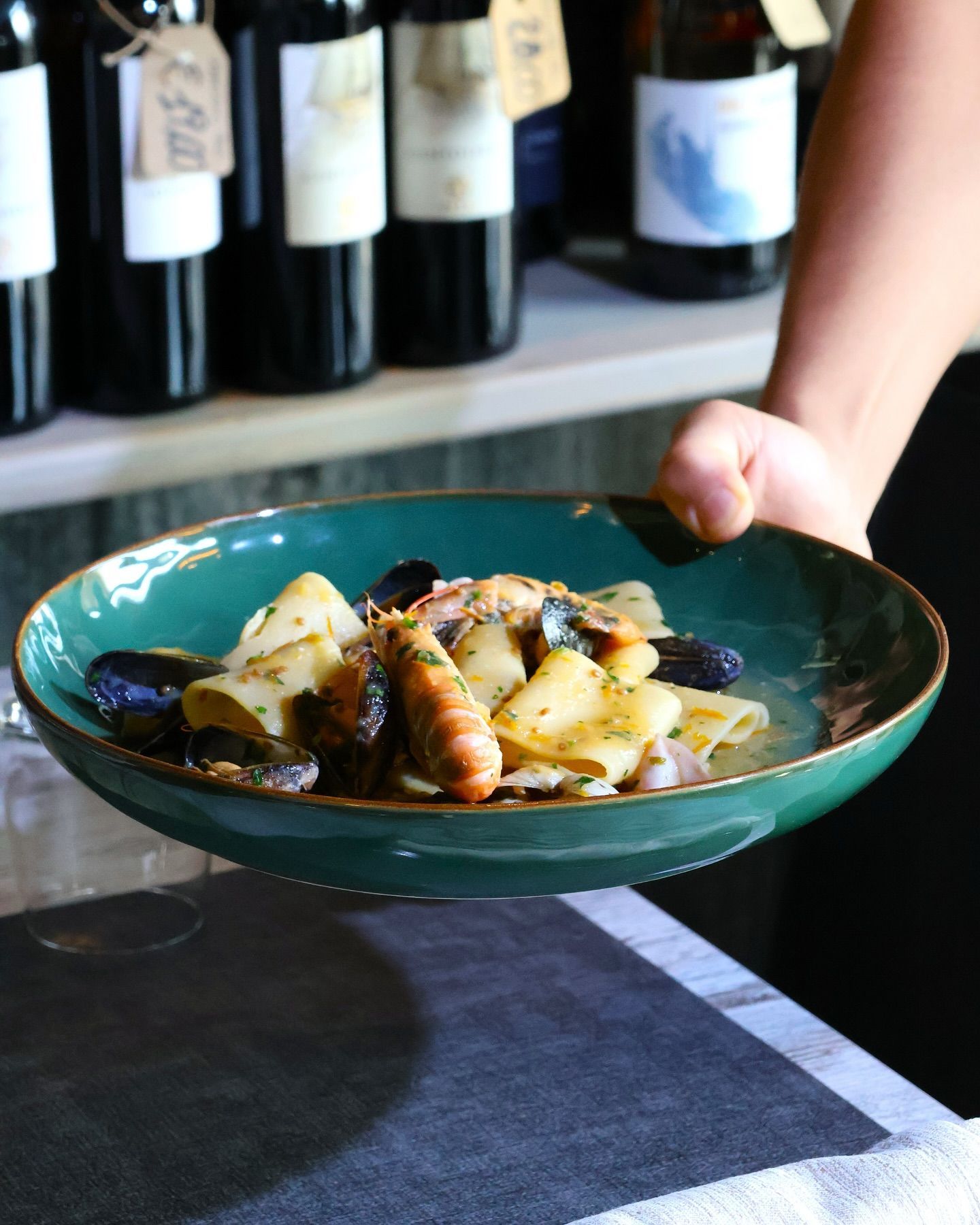 Una persona tiene in mano un piatto di cibo davanti a delle bottiglie di vino.