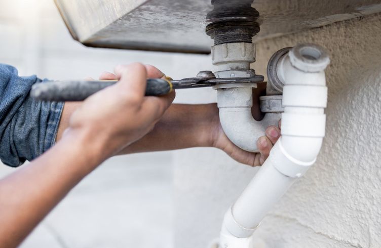A person is fixing a pipe with a wrench.