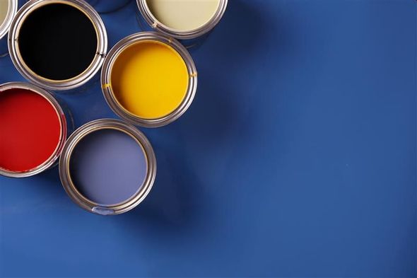 Open paint cans in red, black, yellow, cream, and blue on a blue surface.