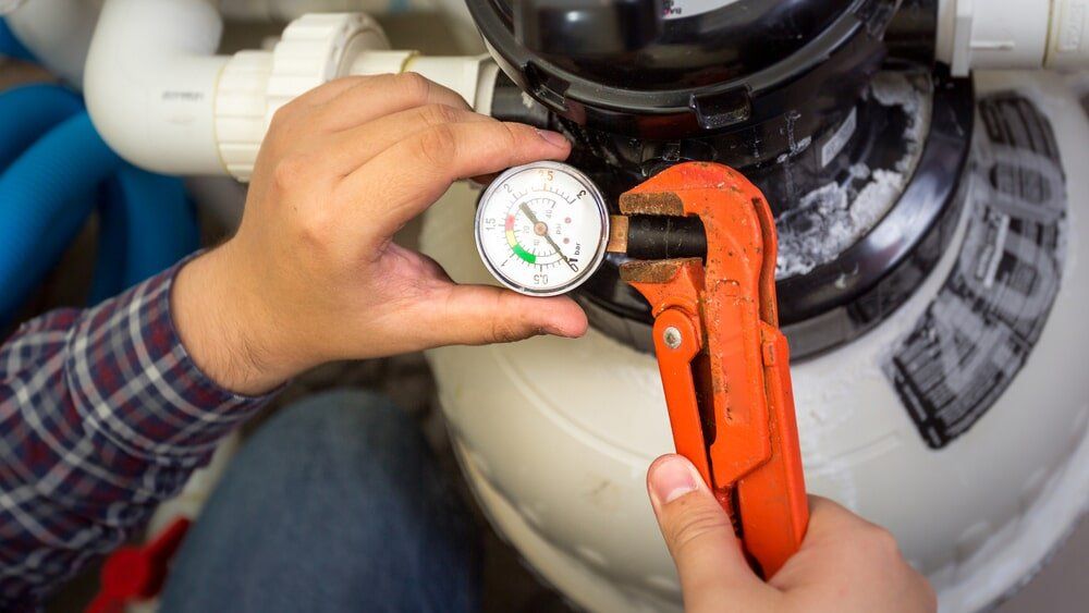 A man is fixing a pool filter with a wrench and a pressure gauge.