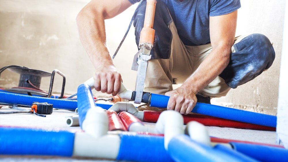 A man is kneeling on the floor working on a pipe.