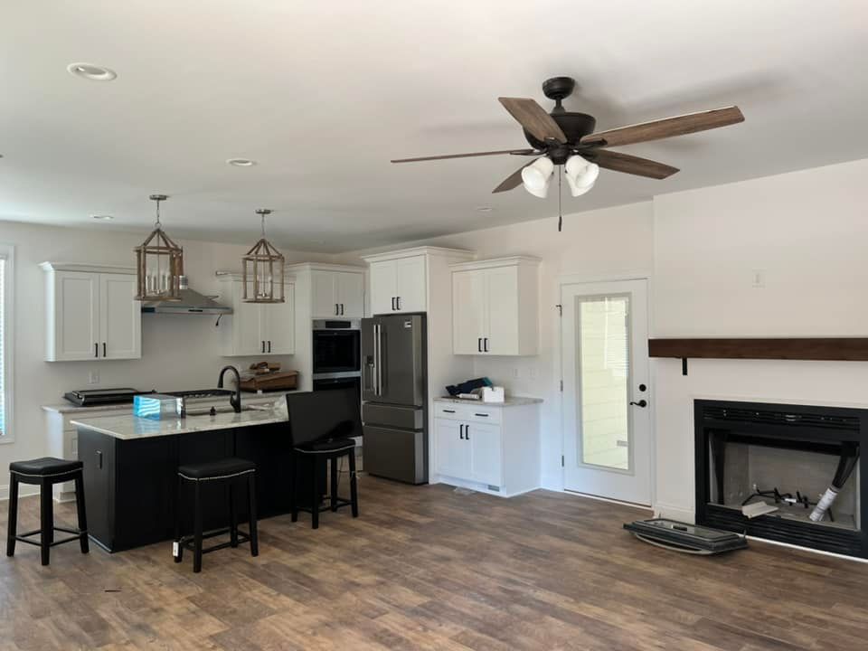 Open kitchen with white cabinets, black island, dark appliances, fireplace, and ceiling fan.