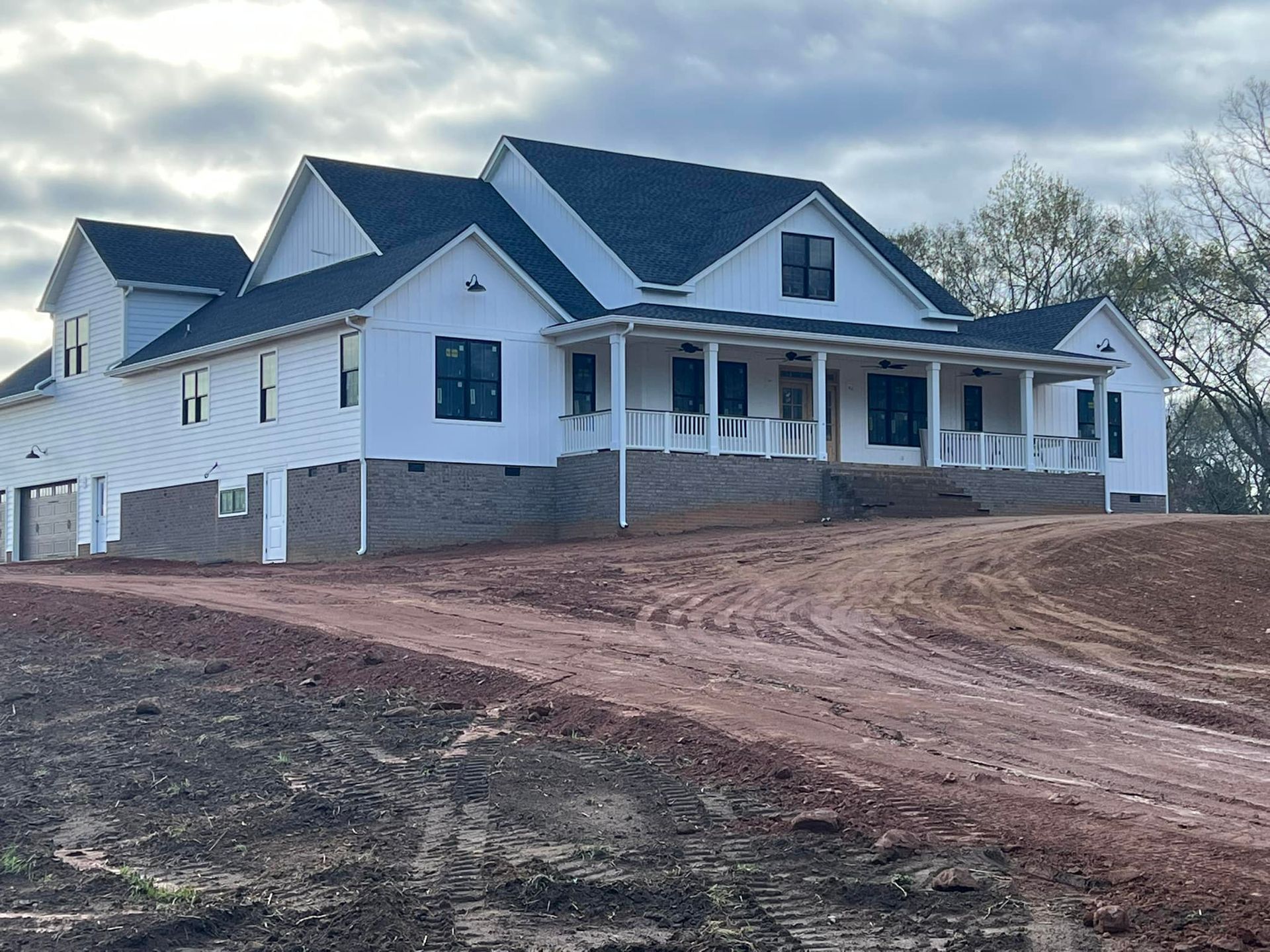 White farmhouse with black trim, a long porch, and a gravel driveway on a slightly sloped lot.