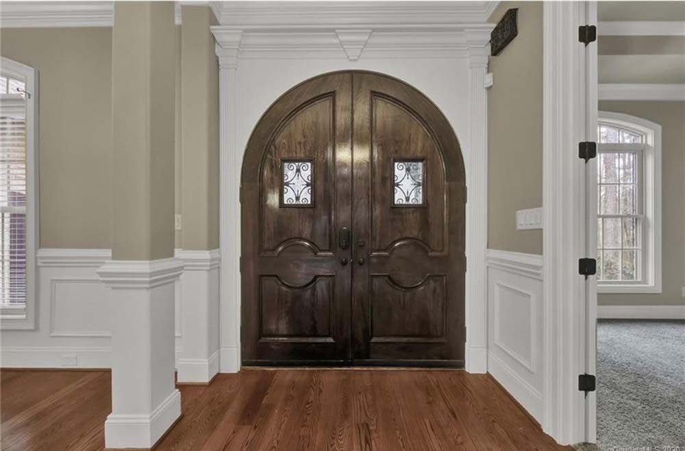 Dark wood arched double doors in a home, with decorative trim and sidelights.