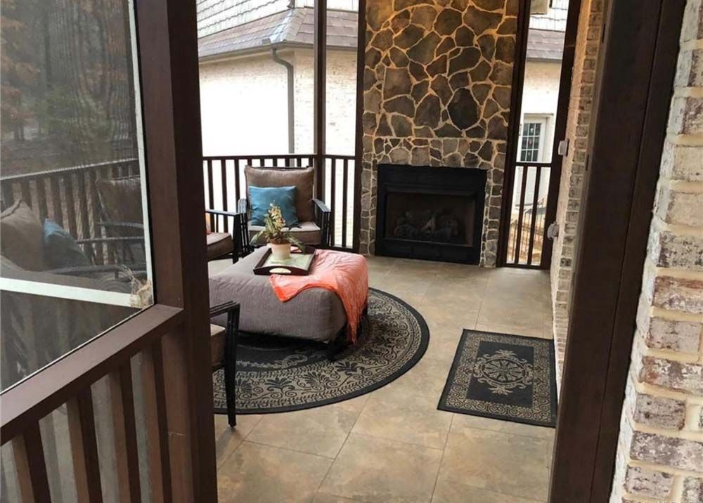 Screened-in porch with fireplace, seating area, and dark wood trim. Features stone wall, rug, and open door.