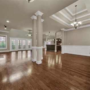 Spacious, empty living room with hardwood floors, two columns, and a chandelier.