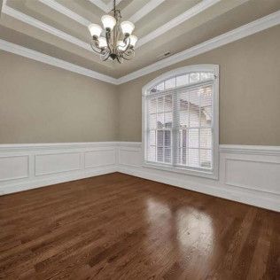 Empty room with dark hardwood floors, white trim, beige walls, and chandelier.