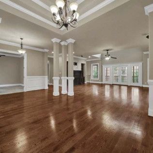 Spacious room with dark wood floor, beige walls, white trim and pillars, chandelier, and french doors.