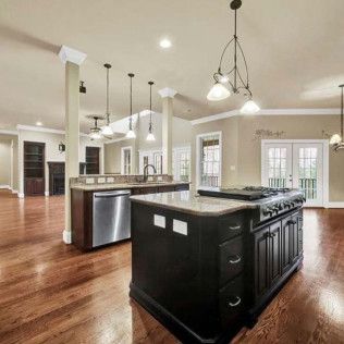 Spacious kitchen with dark wood island and stainless steel appliances, open to living area with hardwood floors.