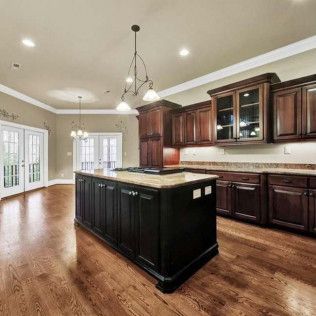 Spacious kitchen with dark wood cabinets, a black island with a cooktop, and hardwood floors.
