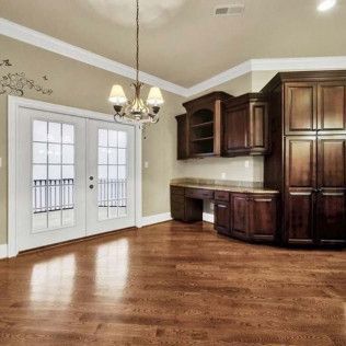 Hardwood-floored room with dark wood cabinets, a desk, and French doors leading to a balcony. A chandelier hangs from the ceiling.