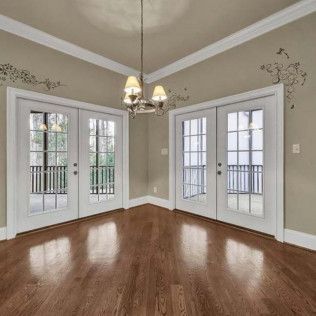 Empty room with hardwood floors, two sets of French doors, and a chandelier; light beige walls.