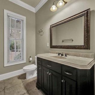 Bathroom with dark wood vanity, large mirror, toilet, and window with blinds.