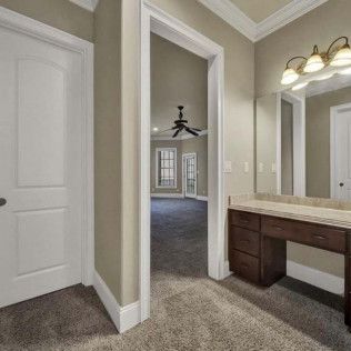 Bathroom with vanity, open doorway to a bedroom, white doors, and tan walls.
