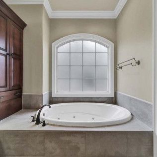 Bathroom with oval tub, built-in storage, and frosted arched window. Neutral tones, tile surround.