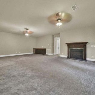 Empty room with gray carpet, fireplace, two ceiling fans, and neutral walls.