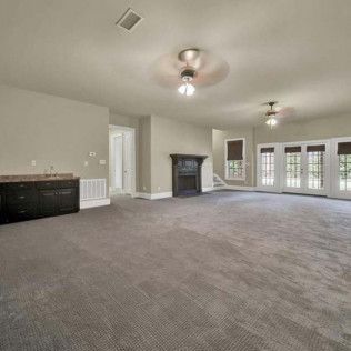 Spacious, empty room with gray carpet, fireplace, dark bar, and French doors to the outside.