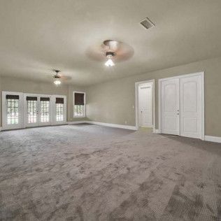 Empty room with gray carpet, two ceiling fans, French doors, and white doors.