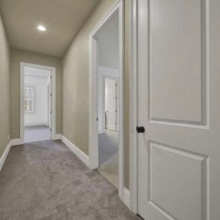 Narrow hallway with carpet, doors, and neutral-colored walls.