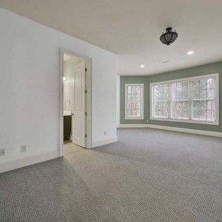 Empty bedroom with gray carpet, white walls, and a green accent wall with windows.