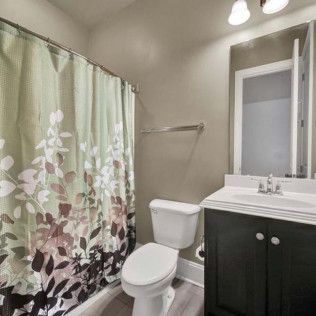 Bathroom with floral shower curtain, toilet, sink, mirror, and dark vanity.