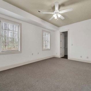 Empty white bedroom with gray carpet, two windows, and a ceiling fan.
