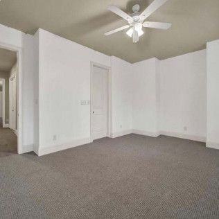 Empty room with white walls, carpeted floor, ceiling fan, and doors.