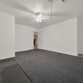 Empty room with gray carpet and white walls. A ceiling fan hangs from the ceiling.