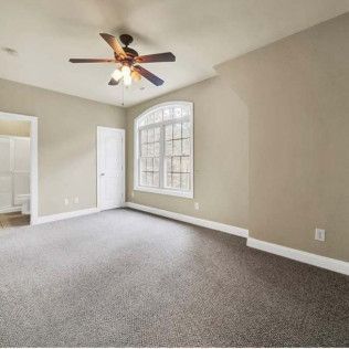 Empty bedroom with gray carpet, a ceiling fan, and a large window.