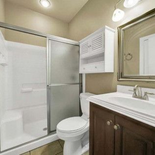 Bathroom with white shower, toilet, sink, and wooden cabinet, with a medicine cabinet and mirror.