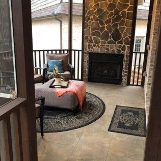 Sunroom with stone fireplace, sitting area, round rug, and an ottoman with a blanket.
