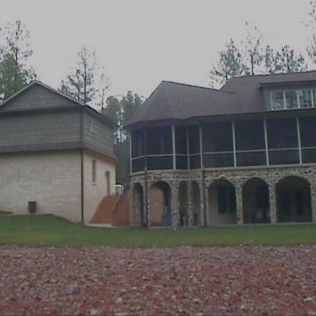 Large house with screened-in porch and stone arches, adjacent to a smaller building; overcast day.