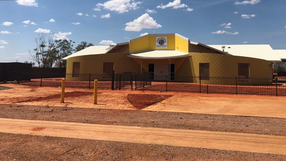 A yellow building with a white roof is surrounded by dirt and a fence.