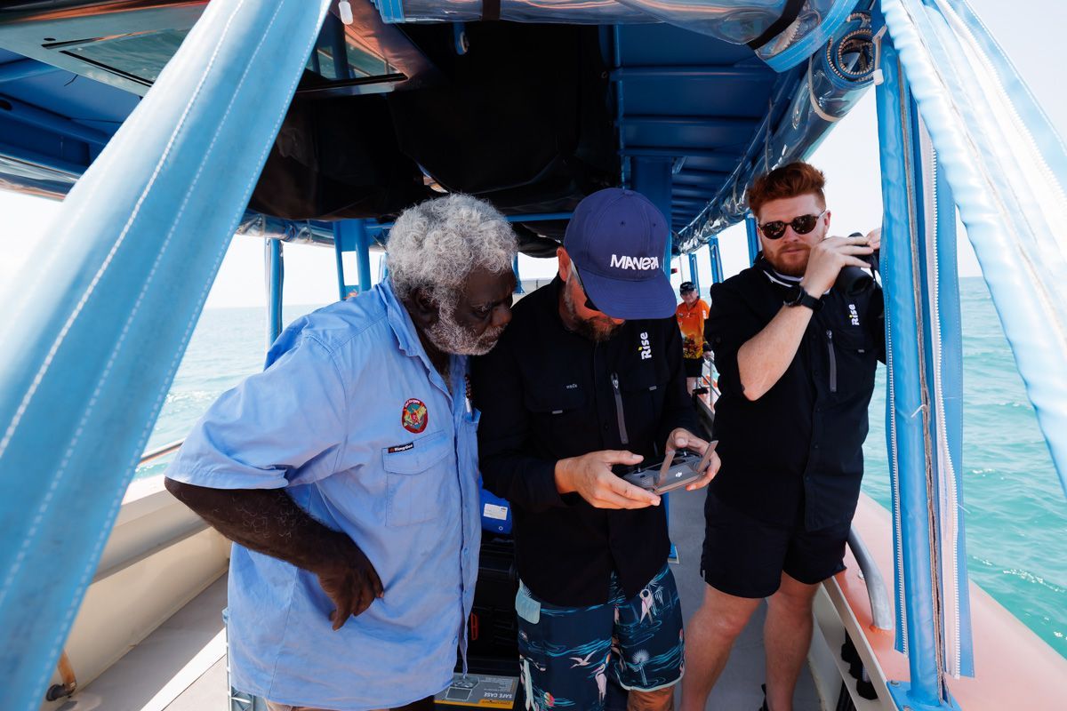 Three men are standing on a boat looking at a remote control.
