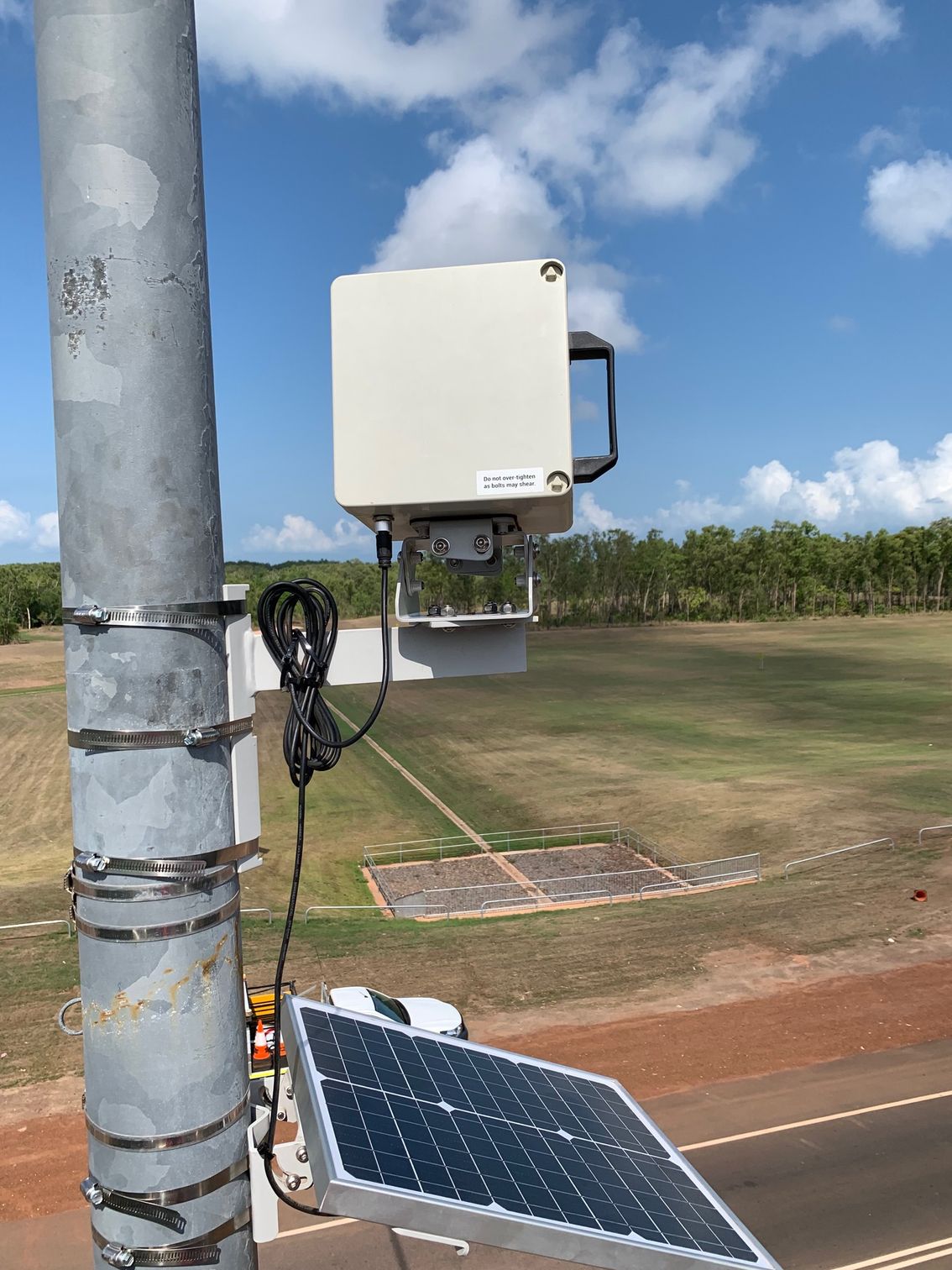 A solar panel is attached to a pole next to a field.