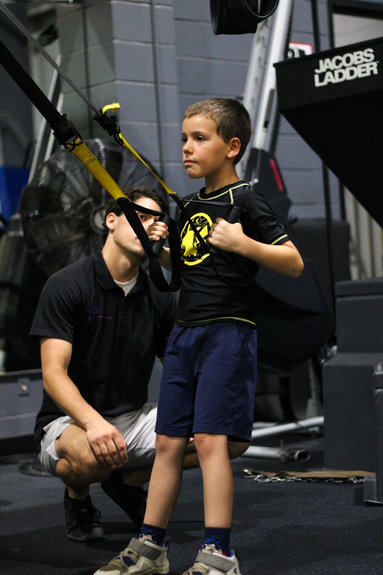 A man is helping a young boy use a trx machine in a gym