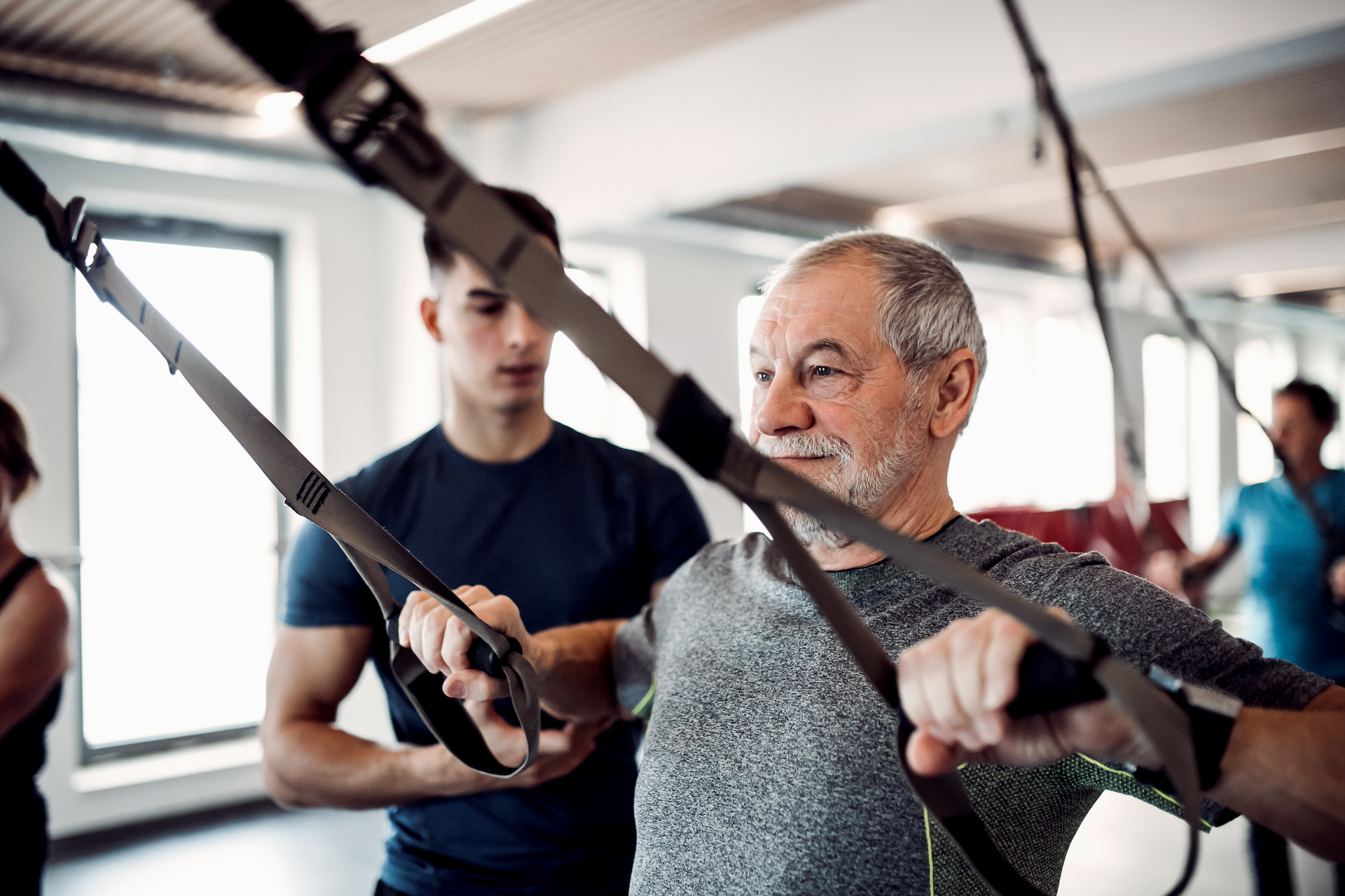 An older man is doing exercises with a trainer in a gym.