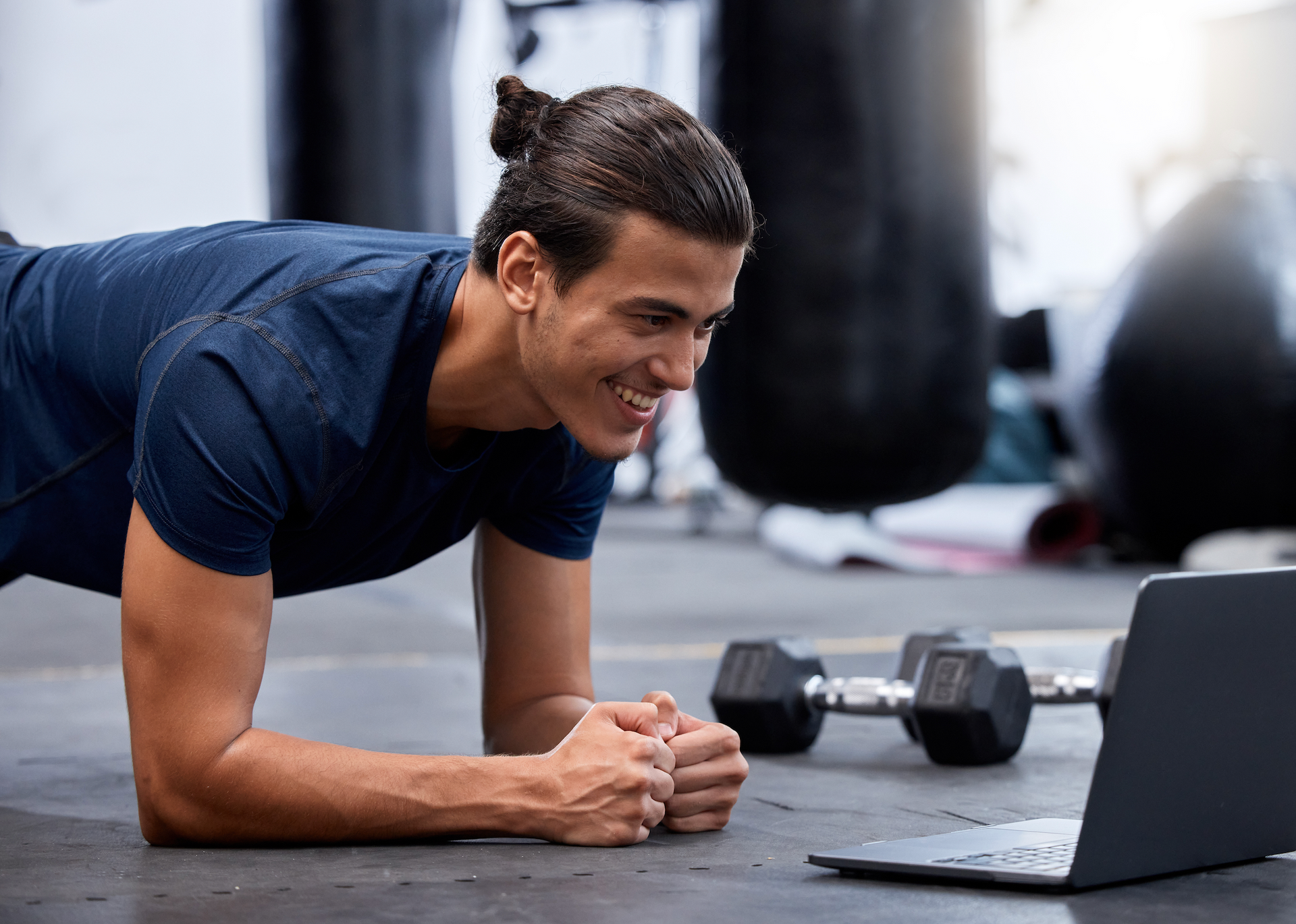 A man is doing a plank while looking at a laptop in a gym.