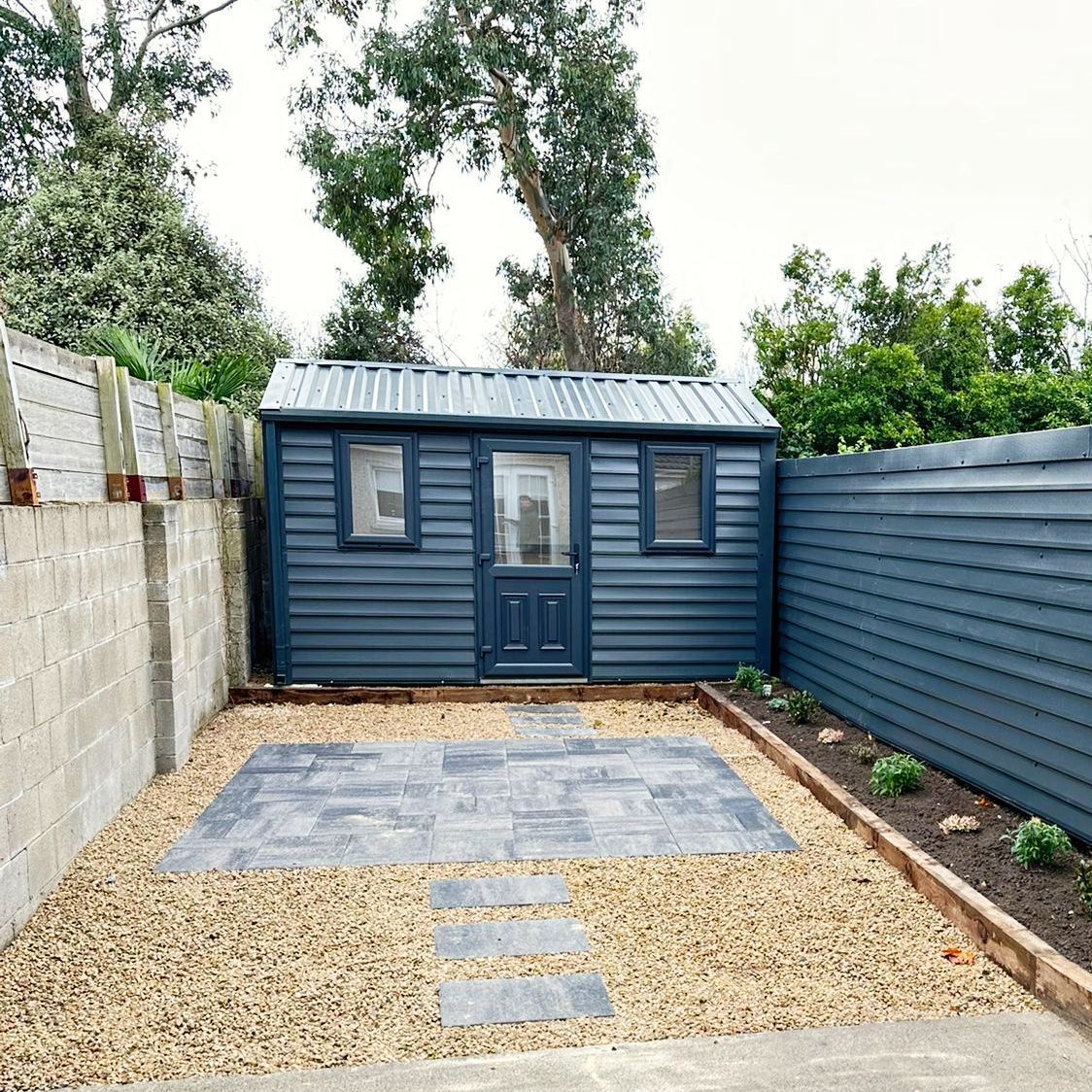Blue shed with gray stone patio, gravel, and wooden fences.
