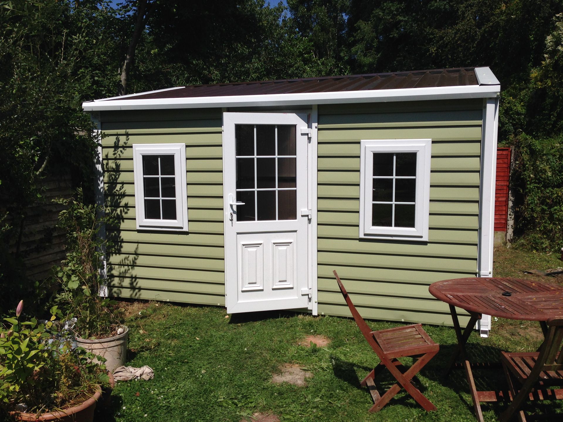 Green garden shed with white trim and a brown roof, door ajar.